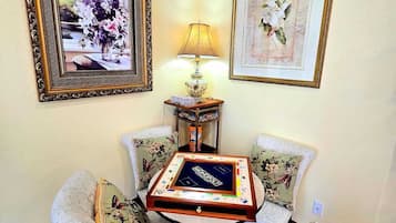 A room with a Monopoly board game on a table, two chairs with floral cushions, a lamp, and two framed pictures on the wall.