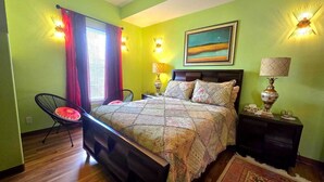 A bedroom with a bed, two bedside tables, a chair, a window with curtains, and a painting on the wall.