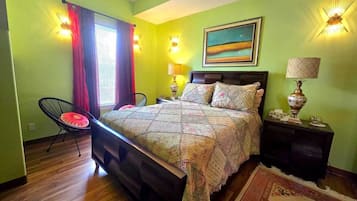 A bedroom with a bed, two bedside tables, a chair, a window with curtains, and a painting on the wall.
