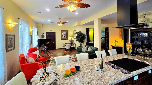 A spacious living area with a large island, a ceiling fan, and a kitchen area with a black range hood.