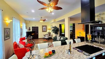 A spacious living area with a large island, a ceiling fan, and a kitchen area with a black range hood.