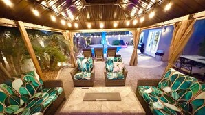 An outdoor seating area with wicker furniture and a central table, surrounded by a covered patio with string lights. - Relaxing & Luxurious Private Oasis w heated Pool/Spa 10 min from Las Vegas Strip (Henderson)