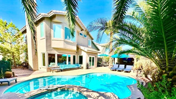 A swimming pool with lounge chairs, a house with a patio, and palm trees. - Relaxing & Luxurious Private Oasis w heated Pool/Spa 10 min from Las Vegas Strip (Henderson)