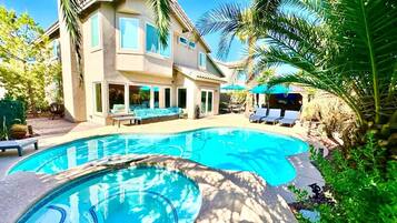 Una piscina con sillones de descanso, una casa con patio y palmeras.