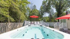 Ein Whirlpool, umgeben von einer Holzterrasse, mit einem weißen Zaun und Bäumen im Hintergrund.
