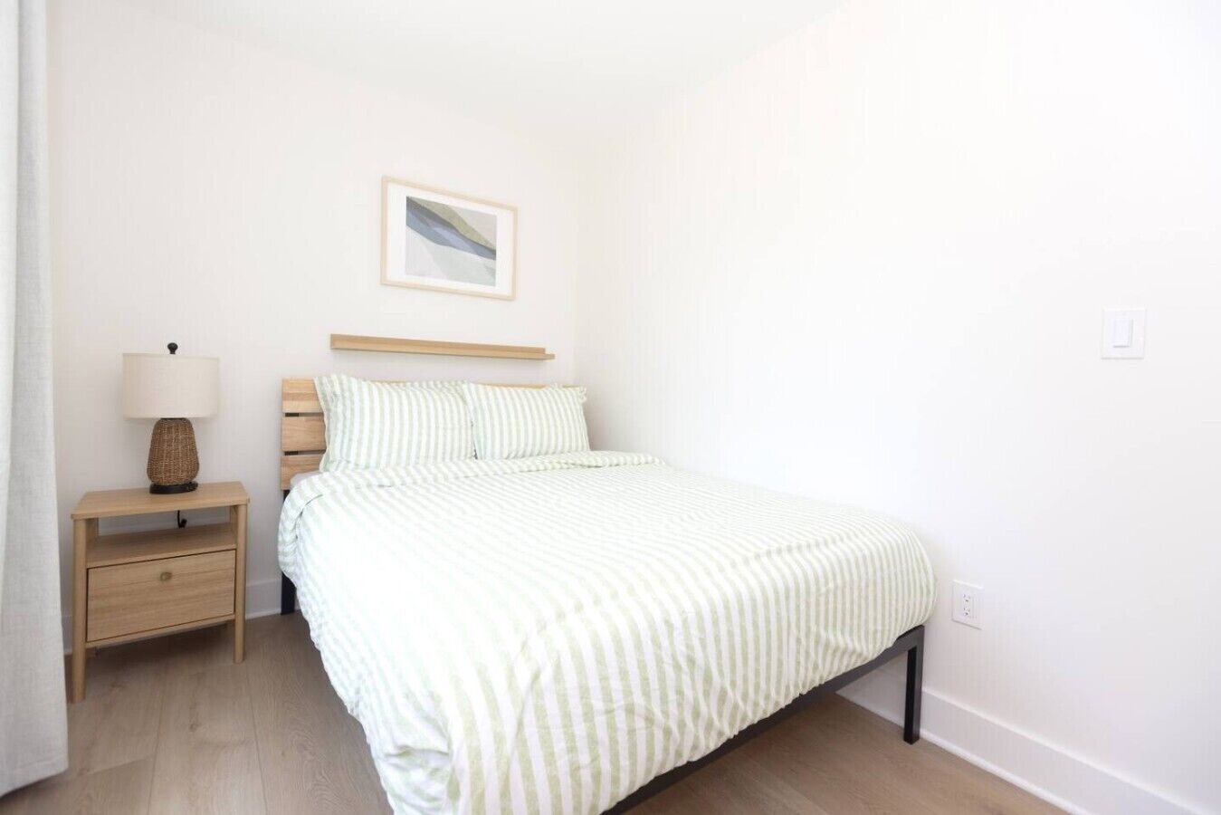 A bedroom with a bed, a nightstand, a lamp, and a framed picture on the wall.