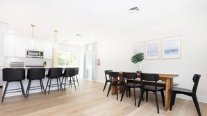 Eine moderne Küche mit weißen Schränken, einer Mikrowelle und einem Essbereich mit einem Holztisch und schwarzen Stühlen.