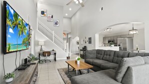 Ein modernes Wohnzimmer mit großem Fernseher, grauem Sofa, Couchtisch aus Holz und einer Treppe zu einer weiteren Ebene.