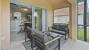 Ein Balkon mit einer Sitzecke, einem Tisch und einer sichtbaren Küchenzeile durch eine Glastür.