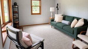 Una sala de estar con un sofá verde, una silla, una lámpara y una ventana.