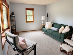 A living room with a green sofa, a chair, a lamp, and a window. - Cozy 3-bedroom house in charming Cedar Falls (Cedar Falls)