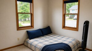 Un dormitorio con cama, dos ventanas y un calefactor.