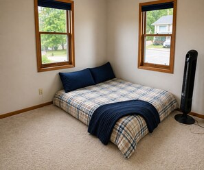 A bedroom with a bed, two windows, and a standing heater. - Cozy 3-bedroom house in charming Cedar Falls (Cedar Falls)