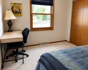 Un dormitorio con escritorio, silla, cama, ventana y puerta.