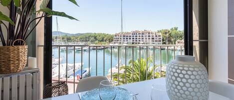 A balcony with a view of a marina, a large vase, and a table with glasses.