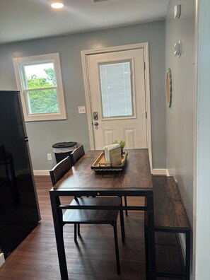A dining area with a dark wooden table, two chairs, a tray with books and a plant, and a window with blinds. - The Arkside Cottage - The ark, creation museum, Williamstown marina (Williamstown)