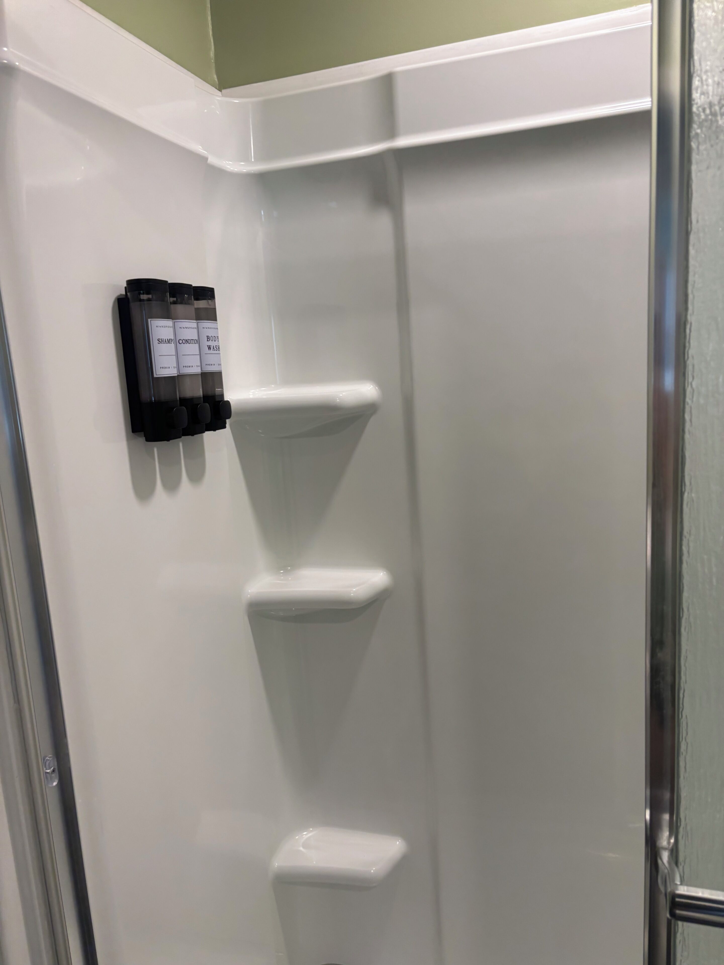 A corner of a bathroom with a white wall, a black soap dispenser, and a white towel rack.
