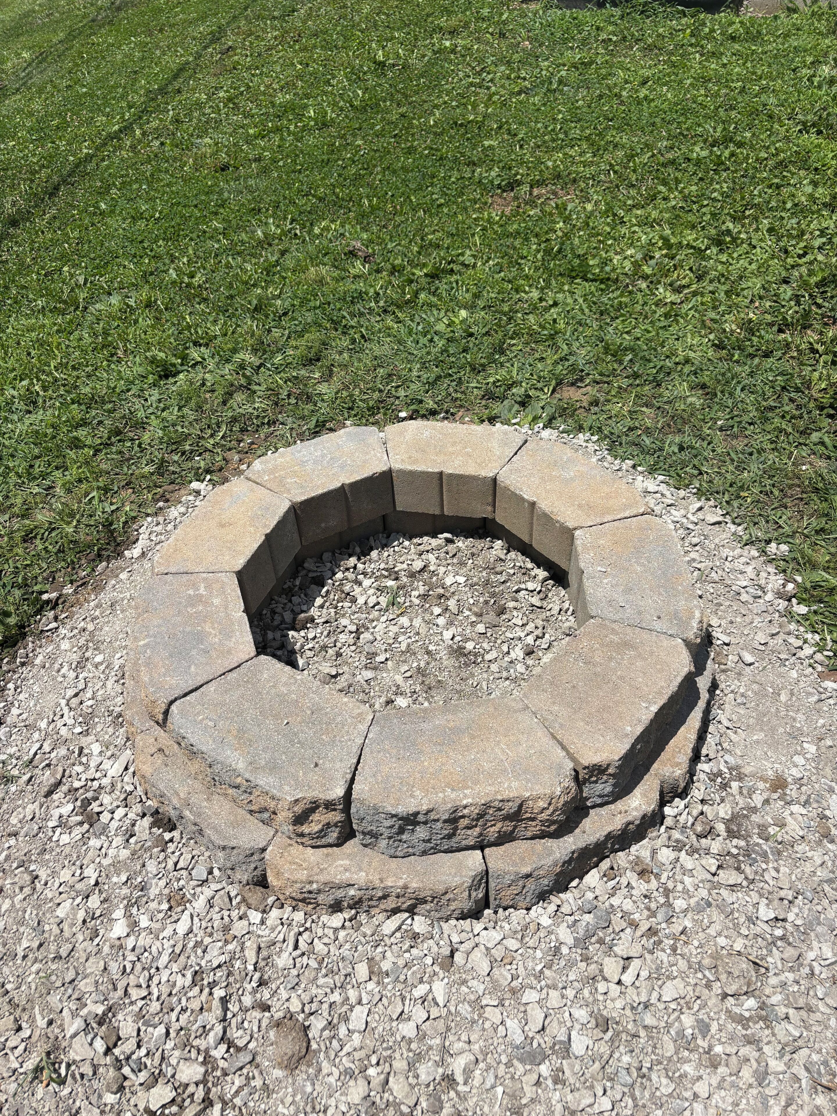 Un foyer circulaire en pierre, entouré de gravier, aménagé dans un espace herbeux.