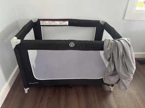 A portable crib with a safety label, wheels, and a mesh panel. - The Arkside Cottage - The ark, creation museum, Williamstown marina (Williamstown)