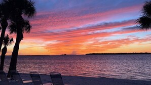 A beach with palm trees, a sunset, and a row of empty beach chairs. - Sanibel Harbour 517:  Luxury Water View! Experience gorgeous corner view! (Fort Myers)