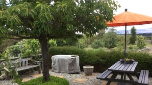Une terrasse de jardin avec une table et un banc, entourée de gravier et de verdure.