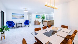 A modern living room with a dining area, featuring a large table, multiple chairs, and a sofa. - Blue Haven Villa /Pool, Hot Tub,Mini Golf & Game Room/ Sleeps 12 (Cape Coral)