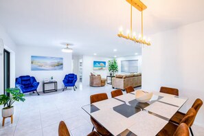 Uma sala de estar moderna com área de jantar, apresentando uma mesa grande, várias cadeiras e um sofá.