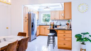 A modern kitchen with wooden cabinets, a stainless steel refrigerator, a dining area with a table and chairs, and a potted plant. - Blue Haven Villa /Pool, Hot Tub,Mini Golf & Game Room/ Sleeps 12 (Cape Coral)