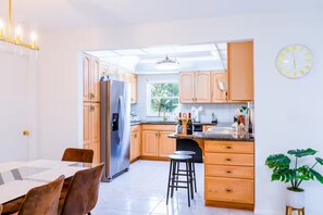 Cozinha moderna com armários de madeira, geladeira de aço inoxidável, área de jantar com mesa e cadeiras, e um vaso com planta.