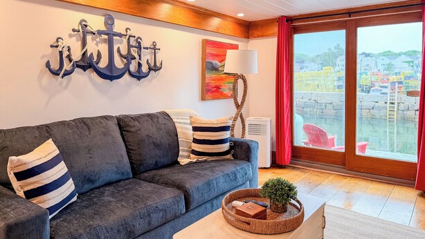 Una sala moderna con un sofá, una mesa de centro, una decoración anclada en la pared, una lámpara y vistas de edificios a través de un ventanal grande.