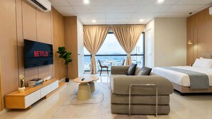 A modern hotel room with a TV displaying 'NETFLIX,' a sofa, a bed, a small table, and a view of the city through large windows. - Edelweiss Tropicana Gardens by Guestonic (Petaling Jaya)