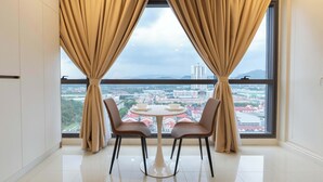 A room with a balcony, two chairs, a table, and a view of a cityscape. - Edelweiss Tropicana Gardens by Guestonic (Petaling Jaya)