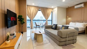 A modern hotel room with a flat-screen TV, a sofa, a bed, a dining area, and a view of the city. - Edelweiss Tropicana Gardens by Guestonic (Petaling Jaya)