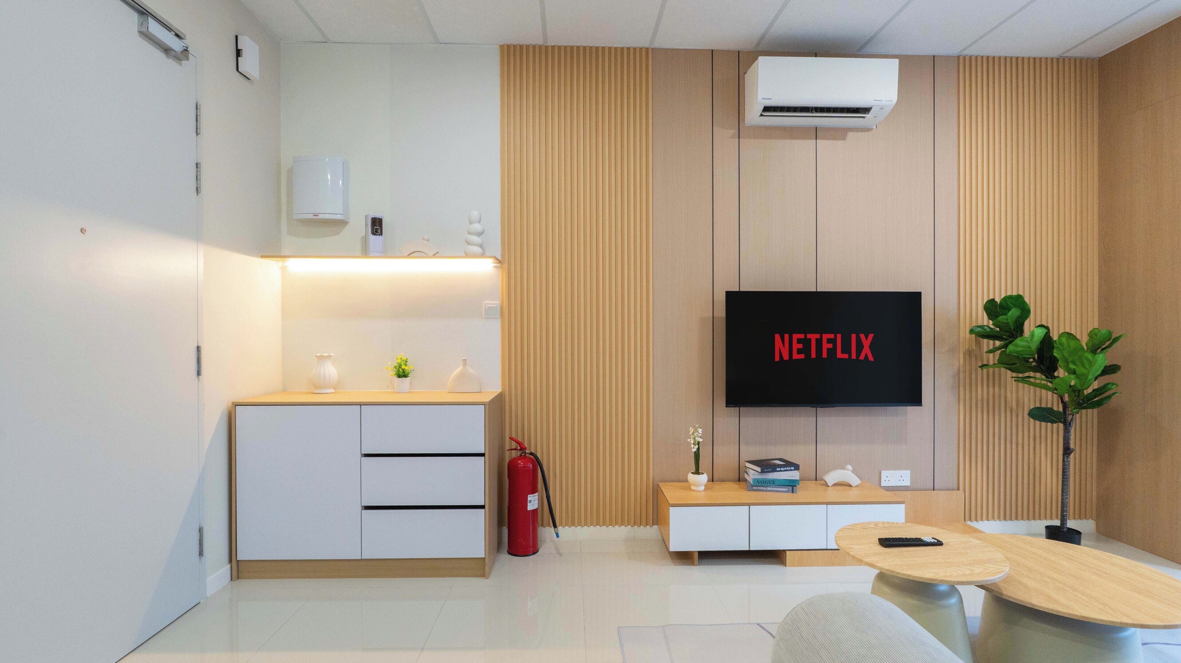 Un salon moderne avec un téléviseur à écran plat affichant le logo « NETFLIX », un canapé blanc, une petite table et une plante.