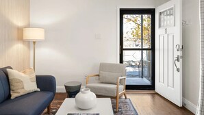 Sala de estar com sofá, poltrona, luminária e vista através de uma porta.
