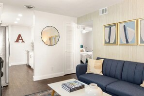 A living room with a blue sofa, a coffee table with a book and a vase, a mirror, and a wall with a large letter 'A'. - Modern 2BR Apartment in Atlanta - Near Beltline & Downtown (Atlanta)