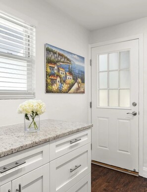 A kitchen with white cabinets, a granite countertop, a vase of flowers, and a painting of a coastal village. - Modern 2BR Apartment in Atlanta - Near Beltline & Downtown (Atlanta)