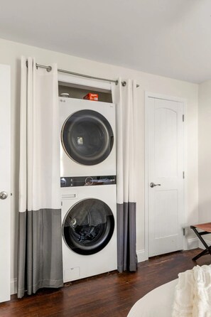 A laundry room with two stacked washing machines, a door, and a wooden floor. - Modern 2BR Apartment in Atlanta - Near Beltline & Downtown (Atlanta)
