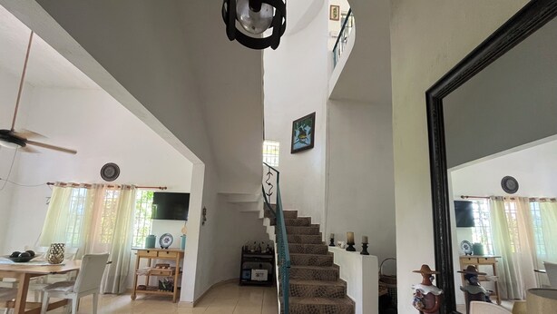 Un'ampia zona giorno con tavolo da pranzo, sedie, una scala e un grande specchio.