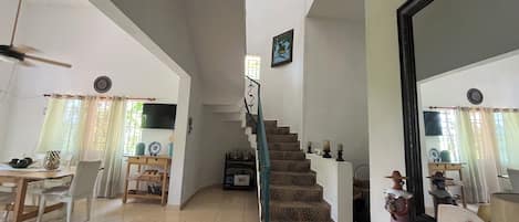Ein geräumiger Wohnbereich mit Esstisch, Stühlen, einer Treppe und einem großen Spiegel.