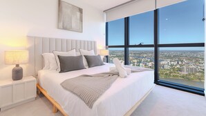 A modern bedroom with a large bed, a nightstand, a lamp, and a city view through large windows. - Sunrise Views on Level 57 | Queen's Wharf King Suite | Pool, Sauna & Parking (Brisbane City)