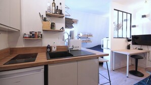 Une cuisine compacte équipée d’un lave-vaisselle encastré, d’un évier et d’une cuisinière. Des étagères au-dessus du plan de travail servent à ranger divers ustensiles de cuisine, et un téléviseur est fixé au mur.