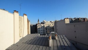 Un toit-terrasse avec une toiture métallique, des bâtiments adjacents et un ciel dégagé.