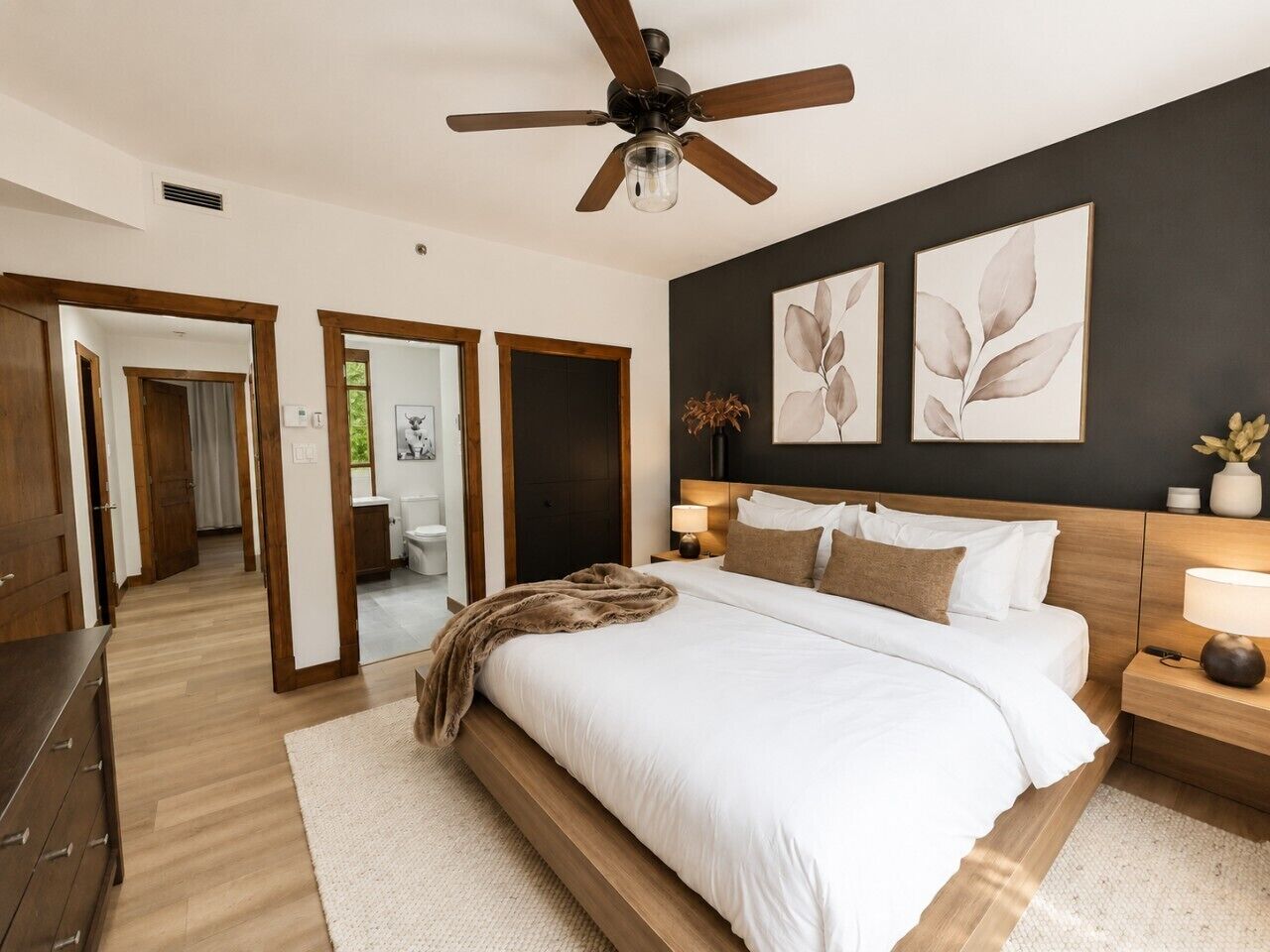 Une chambre à coucher avec un lit, un ventilateur de plafond, une table de chevet et des œuvres d’art accrochées au mur.