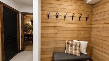 Un mur lambrissé en bois, avec un banc et des coussins, une porte noire et, au fond, un coin repas.