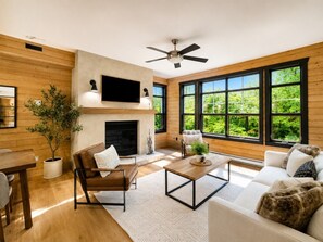 Un salon moderne doté d’une cheminée, de murs en bois, de grandes fenêtres et d’un ventilateur de plafond.