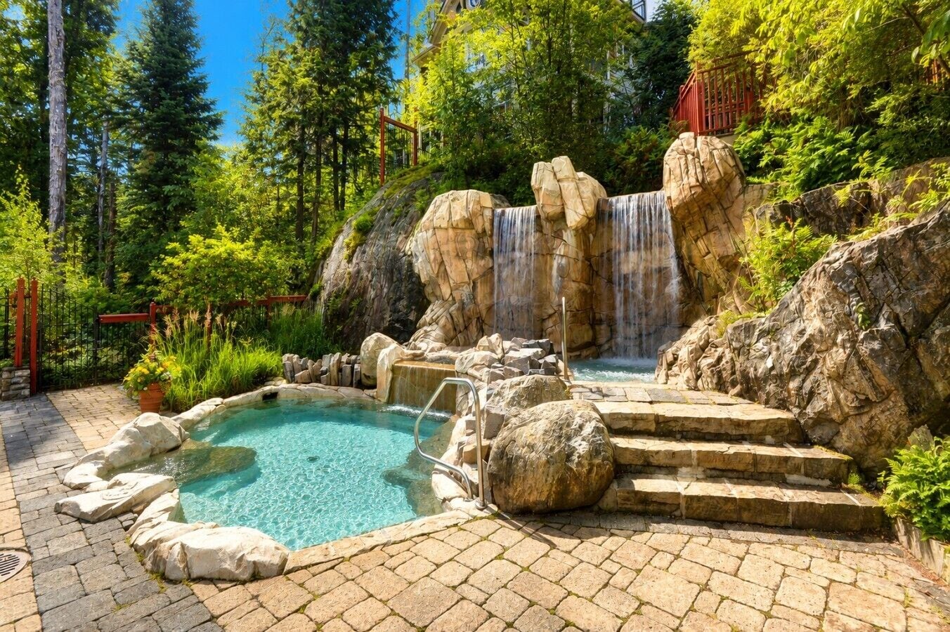 Une piscine naturelle avec une cascade, entourée de rochers et de verdure.