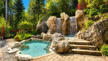 Une piscine naturelle avec une cascade, entourée de rochers et de verdure.