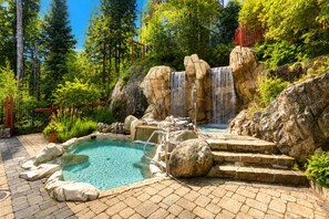 Une piscine naturelle avec une cascade, entourée de rochers et de verdure.