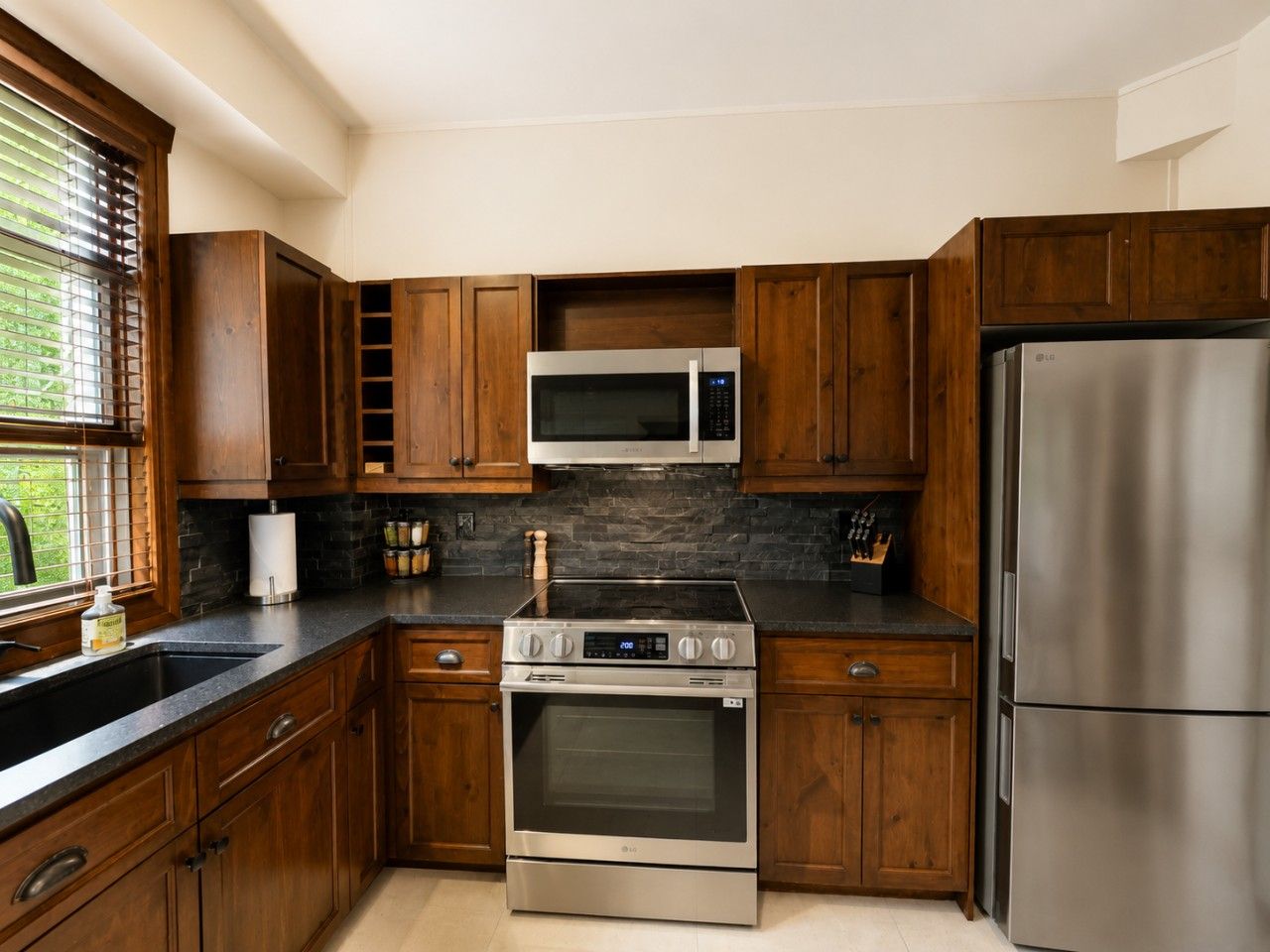 Una cocina con armarios de madera, un refrigerador de acero inoxidable, un microondas, un horno y un lavamanos.